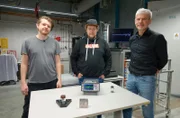 Das Erfinder-Duo Dimitri Benke (links) und Dr. Maximilian Fries aus Darmstadt sowie Prof. Oliver Gutfleisch (rechts). Auf dem Tisch liegt im Vordergrund die Erfindung, das magnetische Kühlsystem, dahinter ein Messgerät. Prof. Gutfleisch wird Erfindung testen.