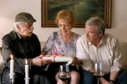 Edwin Bremer (Tilo Prückner, l.) schenkt Heidrun (Verena Plangger, M.), der Frau seines Kollegen Günter Hoffmann (Wolfgang Winkler, r.) ein Fotobuch.