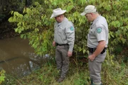 Two wardens looking down into a small pond.  Daniel Roraback (r.)