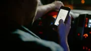 Ein Mann sitzt in einem Auto, hält ein Telefon in der Hand und beobachtet die Route mithilfe der Kartenanwendung.