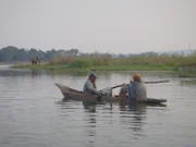 Cody Lundin and Joe Teti in canoe, Cody Lundin points to elephant in the background, Joe Teti holds up fish he caught.
