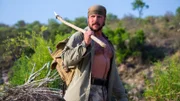 Joe Teti walking along bushes with his backpack and spear.