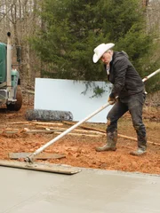 Marty is smoothing out concrete with a large tool that resembles a mop.