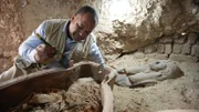 Die Archäologin Bahaa Gaber staubt vorsichtig Sand von dem Sarg ab, der in der Grabstätte von Bahaa Gaber in Dra' Abu el-Naga, Ägypten, gefunden wurde.