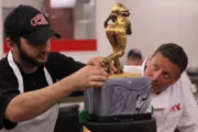 Ralph securing roller girl statue to cake whit Joe watching.