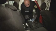 Ein Polizist kontrolliert eine Tasche in einem Auto.