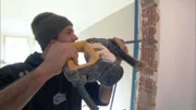 Ingo vom ZiG-Team geht mit schwerem Gerät gegen die Mauer vor..