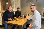 In Münster probiert Björn Freitag (l.) bei Restaurantbereiber Mike Gottlob (m.) und Koch Gentian Koçi (r.) eine Fusion-Burger-Kreation.