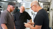 Chef Robert Irvine talks with Blake, son of Mark/ sous chef at Steak N' Stuff, in the kitchen of the restaurant. They are joined by Mark Lelushce, owner of Steak N' Stuff; as seen on Food Network's Restaurant:Impossible Season 20.