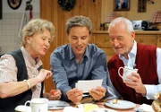 Martin (David Paryla, M.) präsentiert Hildegard (Antje Hagen, l.) und Alfons (Sepp Schauer, r.) Fotos seines Patenkindes.