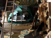 A view within the Amaral barns, an old car in the background amongst scattered papers and debris.