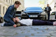 Kris Haas (Jascha Rust, li.) schlendert am Nachmittag durch die Stadt, als er Sanna Lichtenhagen (Diane Willems, liegend) vor ein Auto laufen sieht. Der Fahrer (Frank Haberland, re.) ist schockiert. Kris ist sich sicher, dass dies kein Unfall, sondern Sannas Absicht war.