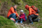Die aufgeweckte Tamara Gotthart (Rosa Wirtz) ist den Berghang hinabgerutscht. Dr. Martin Gruber (Hans Sigl, l.) und Hans Gruber (Heiko Ruprecht, r.) sind schnell vor Ort und kümmern sich um sie.