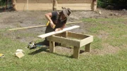 A wide shot of Misty in action as she screws in a new board onto her table project.