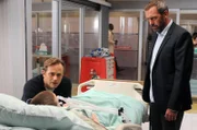 Als House (Hugh Laurie, r.) Roy Randall (Lee Tergesen, l.) das baldige Sterben seines Sohnes Jack (Tanner Maguire, lieg.) ankündigt, will dieser das nicht wahrhaben und glaubt, mit Hilfe des Karmas seinen Sohn retten zu können.