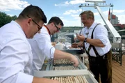 Marcus Kirchgäßner grillt auf dem Sonnendeck Würste. Rudi van der Meulen probiert diese.