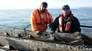 L-R: Juan Ibarra und Freddy Dodge tragen Schwimmwesten, während sie auf einem Boot stehen.