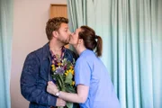 Die Überraschung ist geglückt: Andrea (Anne Weinknecht) schwebt auf Wolke sieben, als ihr Mann Michi (Nils Dörgeloh) sie mit einem riesigen Blumenstrauß bei der Arbeit besucht.