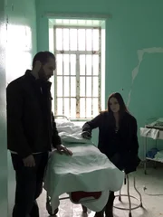 Hosts Nick Groff and Katrina Weidman near a hospital bed in a green room.