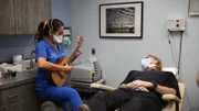 Dr. Lee spielt ihre Ukulele für Jerry Harrison nach dessen Lipom-Entfernung an der Wange.