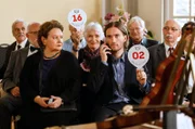 Hannah (Swetlana Schönfeld, li.) beobachtet, wie ein junger Mann (Michael von der Brelle, mi.) ein Gebot auf die Geige abgibt (mit Komparsen), der seine Anweisungen per Telefon erhält.