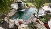 The completed pool area in the backyard of a property with a waterfall, garden and entertainment area.