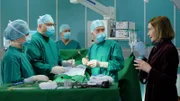 Hans-Peter Brenner (Michael Trischan, 2.v.li.) operiert gerade mit Dr. Kaminski (Udo Schenk, 2.v.re.) als plötzlich eine Patientin einfach im OP steht. Elsa Brandstetter (Gudrun Gundelach, re.) scheint verwirrt zu sein. Kaminski ist fassungslos und bittet Brenner, die Dame sofort aus dem OP zu bringen und sich um sie zu kümmern.