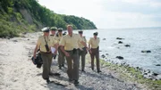 Verdächtige gibt es einige, doch keinen konkreten Beweis. Noch einmal soll der Strand auch im weiteren Umfeld des Tatorts abgesucht werden. Polizist Pöhlmann (Dominic Boeer, 3.v.r.) leitet die Suchaktion. Wird er den entscheidenden Hinweis finden?