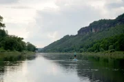 Wanderführerin Kristin Arnold paddelt nach Feierabend auf der Elbe. Das Elbsandsteingebirge bildet mit seinen Felsformationen eine atemberaubende Kulisse.