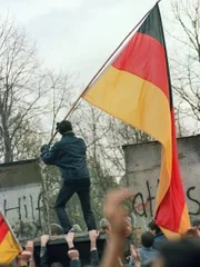 West Berliner prepares to hand over a FRG flag to East German Vopos through a portion of the fallen Berlin Wall near the Brandenbourg Gate early 11 November 1989. Two days before, Gunter Schabowski, the East Berlin Communist party boss, declared that starting from midnight, East Germans would be free to leave the country, without permission, at any point along the border, including the crossing-points through the Wall in Berlin. The Berlin concrete wall was built by the East German government in August 1961 to seal off East Berlin from the part of the city occupied by the three main Western powers to prevent mass illegal immigration to the West. According to the "August 13 Association" which specialises in the history of the Berlin Wall, at least 938 people - 255 in Berlin alone - died, shot by East German border guards, attempting to flee to West Berlin or West Germany. (Photo credit should read GERARD MALIE/AFP/Getty Images)  NO MODEL RELEASES FOR IMAGE.