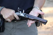 A close-up of a flintlock pistol in Sean Rich's hands as he expertly inspects it.