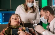 Frieda Müller (Lorna zu Solms, li.) kommt mit Hundebissverletzungen in die Sachsenklinik. Dr. Kai Hoffmann (Julian Weigend, re.). versucht herauszubekommen, wie es dazu kam, doch Frieda will nicht mit der Sprache rausrücken. Sie muss in jedem Fall geröntgt werden und die Wundränder müssen im OP gereinigt werden. Er bittet Schwester Miriam (Christina Petersen, mi.) alles zu veranlassen.