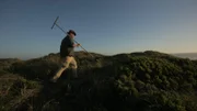 Josh Gates spaziert bei Sonnenuntergang an der Bucht entlang.