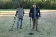 Gastgeber Josh Gates und Metalldetektorexperte Jeff Morgan gehen auf einem Feld auf die Suche nach Metall.