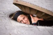 Kalle (Isabelle Höpfner) hebt den Kanaldeckel, um die Lage für ihre Flucht zu checken...