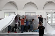 Gemeinsam mit dem Künstler Frank Bölter testen 13 Bremer Kinder, ob sie auch einen megagroßen Papierbogen zu einem Papierschiff falten können.