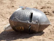 A majestic helmet lays in the dust after a joust.