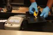 CBP Supervisory Officer Keller benutzt einen Kartonschneider, um ein Pulver, bei dem der Verdacht besteht, dass es sich um Betäubungsmittel handelt, in ein Gemini-Testgerät zu befördern, nachdem es in der Auskleidung eines verschifften Ottomans in Philadelphia gefunden wurde. (National Geographic)