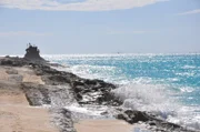 Bimini, Bahamas: Wellen brechen am Strand mit einem Schiffswrack im Hintergrund.