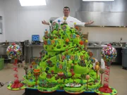 Wide shot of finished Carlo’s Birthday cake, Buddy stands behind.