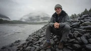Landscape MS of Jeremy Wade sitting on rocks by a river in low light in the bay. Location: Port Fidalgo, Prince William Sound, Alaska.