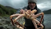 Landscape MS of Jeremy Wade crouching down holding a spider crab to the camera against a moody sky. Crab in focus, Jeremy out of focus.