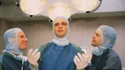 Dr. Schmidt (Walter Sittler) läßt sich gerne von seinen Assistenten (Roland Jankowsky, Alexander Schottky) für sein medizinisches Können bewundern.