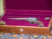 The Priest Colt in its display case along with bullets and a sherrif's badge.