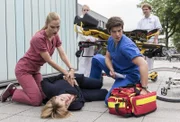 Die Angst-Patientin Birgit Paschke (Winnie Böwe, M.v.) wollte vor ihrer OP fliehen. Vor der Klinik bricht sie zusammen. Julia Berger (Mirka Pigulla, l.) und Ben Ahlbeck (Philipp Danne, r. mit Komparsen, h.) kümmern sich um sie.