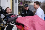 Der wegen Totschlag verurteilte Dennis Karow (Ilja Roßbander, li.) hat sich bei einem Fluchtversuch aus der JVA schwer verletzt. In Begleitung eines Polizisten (Komparse, mi.) wird er in der Sachsenklinik an Dr. Kai Hoffmann (Julian Weigend, re.) übergeben.