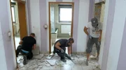Eduard Wittenberg entfernt im Wohnungsflur Fliesen, Thomas Wittenberg und Mike Schopp reißen Türzargen heraus