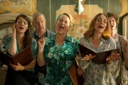 Carola (Julia Hartmann, l.), Christel (Floriane Daniel, M.), Irmela (Julia Richter, r.) und weitere Chormitglieder sind voller Begeisterung bei der Chorprobe.