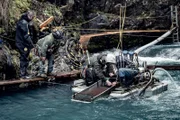 Dustin Hurt and Carlos Minor standing by the edge of the dive site looking at James Hamm and Wesley Richardson searching the sluice box.