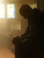 Man sits in church pew and bows his head